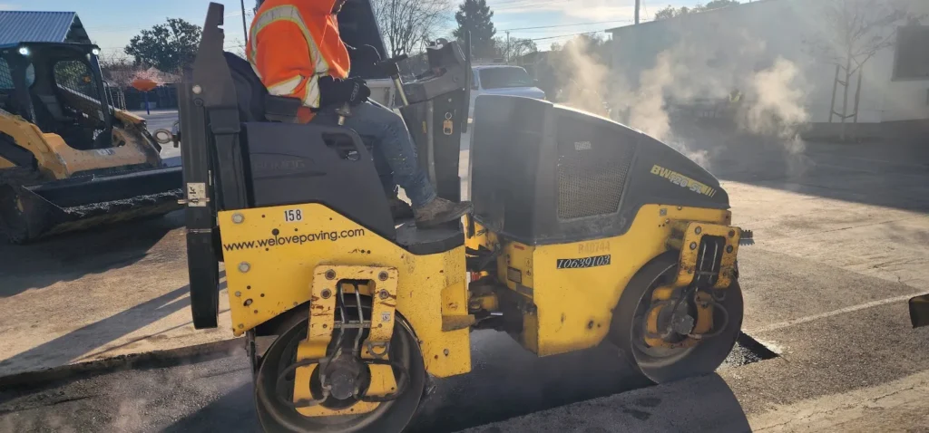 House of Worship Driveway Repair 1 A worker operating a yellow BOMAG steam roller to compact fresh steaming asphalt in Dublin, California. Project by We Love Paving in Dublin, CA.