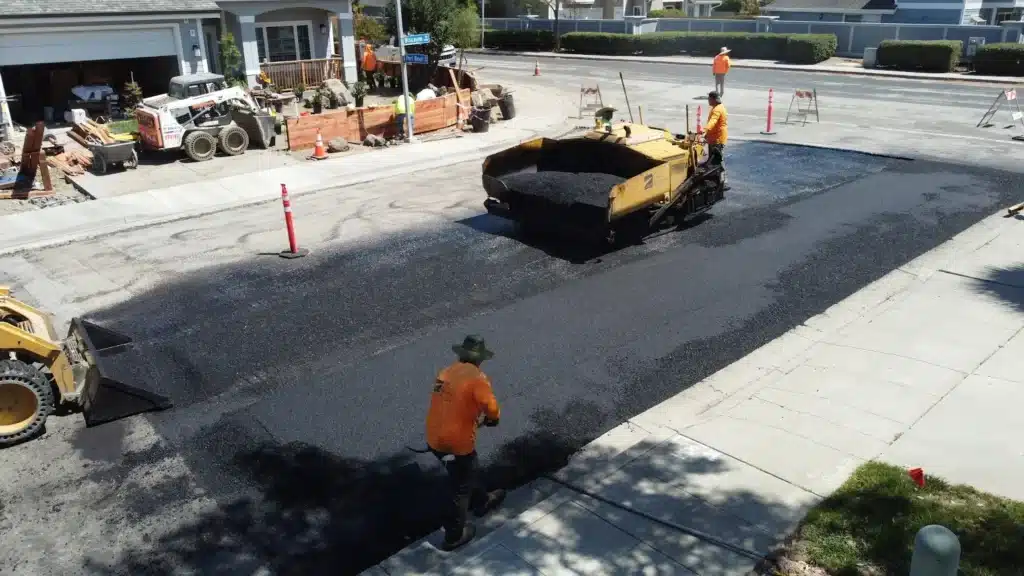 Asphalt Paving 2 A worker in a safety vest using an orange plate compactor on a fresh asphalt patch. Project by We Love Paving in Hayward, CA.