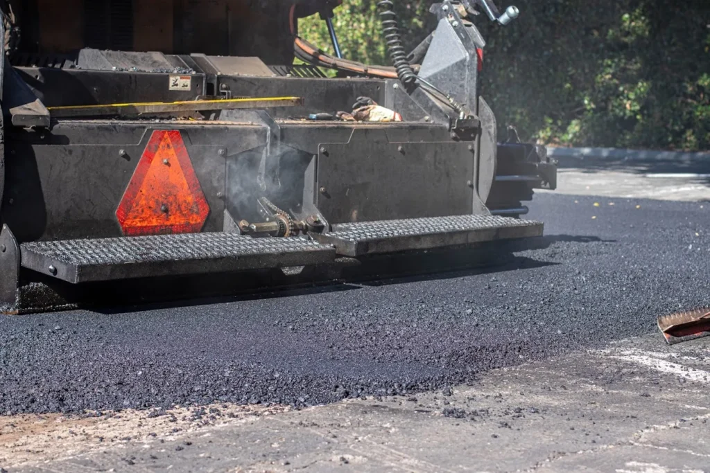 City Street Maintenance in California 1 Close-up of a paving machine laying fresh, steaming black asphalt on a road project in Mill Valley. Project by We Love Paving in Mill Valley, CA.
