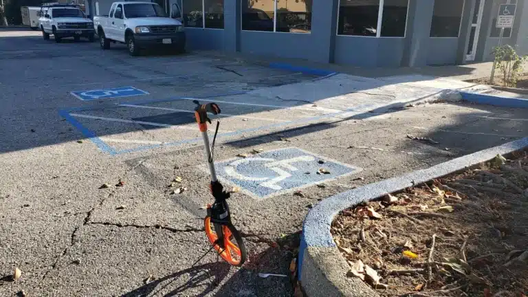 An orange measuring wheel standing on old asphalt next to faded ADA parking symbols and a blue curb. Project by We Love Paving in Northern California, CA.