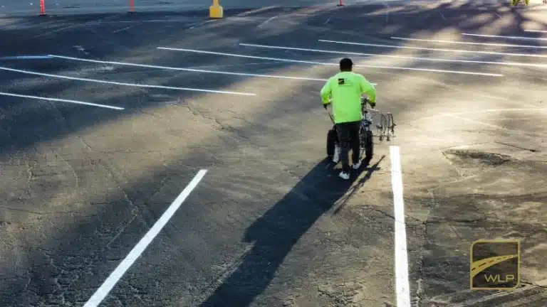 A worker using a walk-behind machine to paint fresh white lines in an asphalt parking lot. Project by We Love Paving in Northern California, CA.