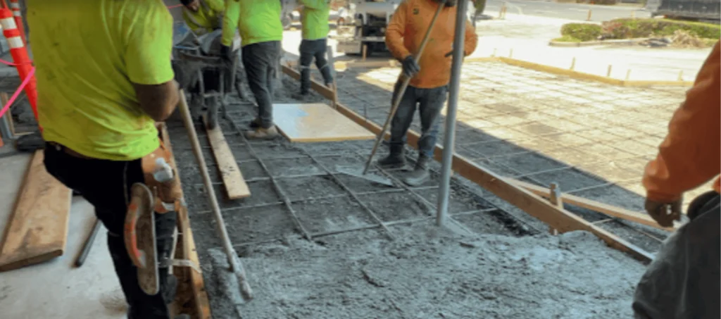 Concrete Contractors 2 A construction crew spreading and leveling wet concrete over a rebar grid for a new pavement project.