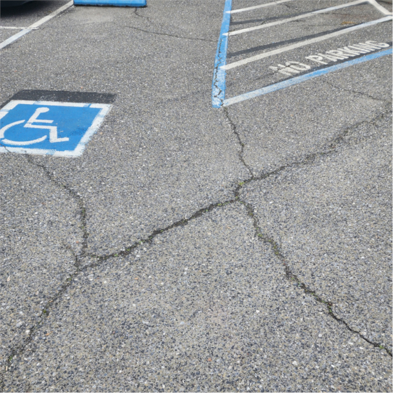 Why Is Parking So Expensive? The Hidden Cost of ADA Parking Lot Issues 1 Cracked asphalt with parking spaces visible.