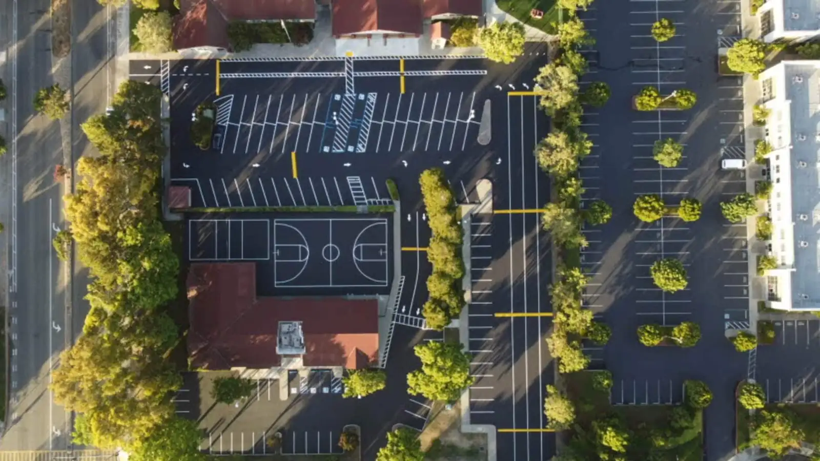 Top-down drone view of a freshly striped school parking lot and basketball court at golden hour in California